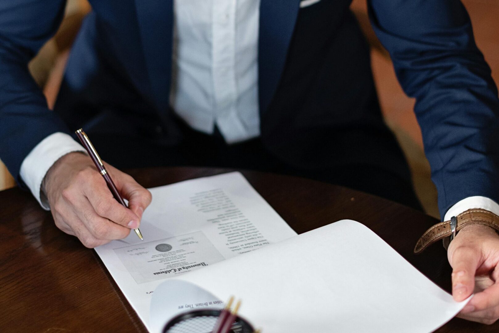 A man in a suit is signing a document at a desk, focused on the task at hand