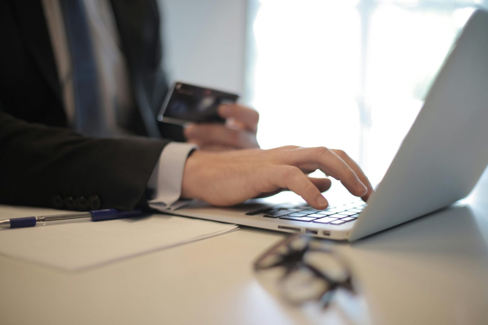 A person in a suit is focused on typing on a laptop at a desk, surrounded by office items
