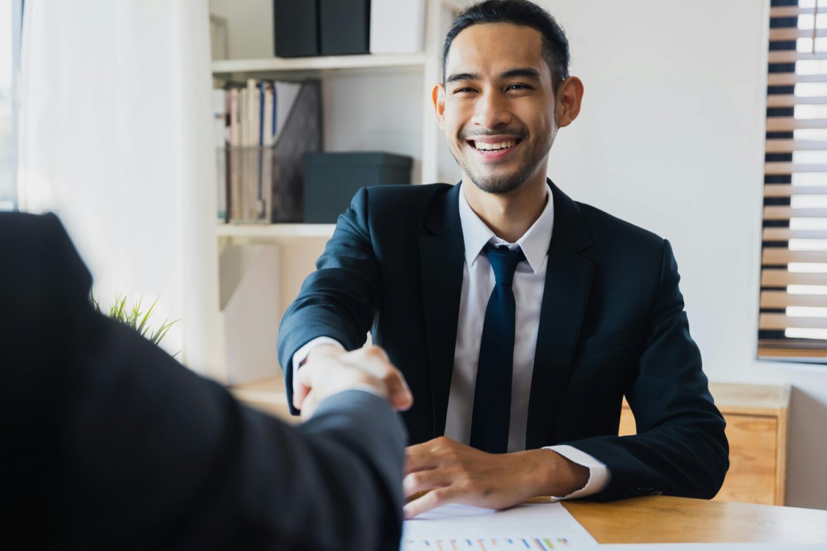 A man in a suit shakes hands with another man, symbolizing a professional agreement or greeting