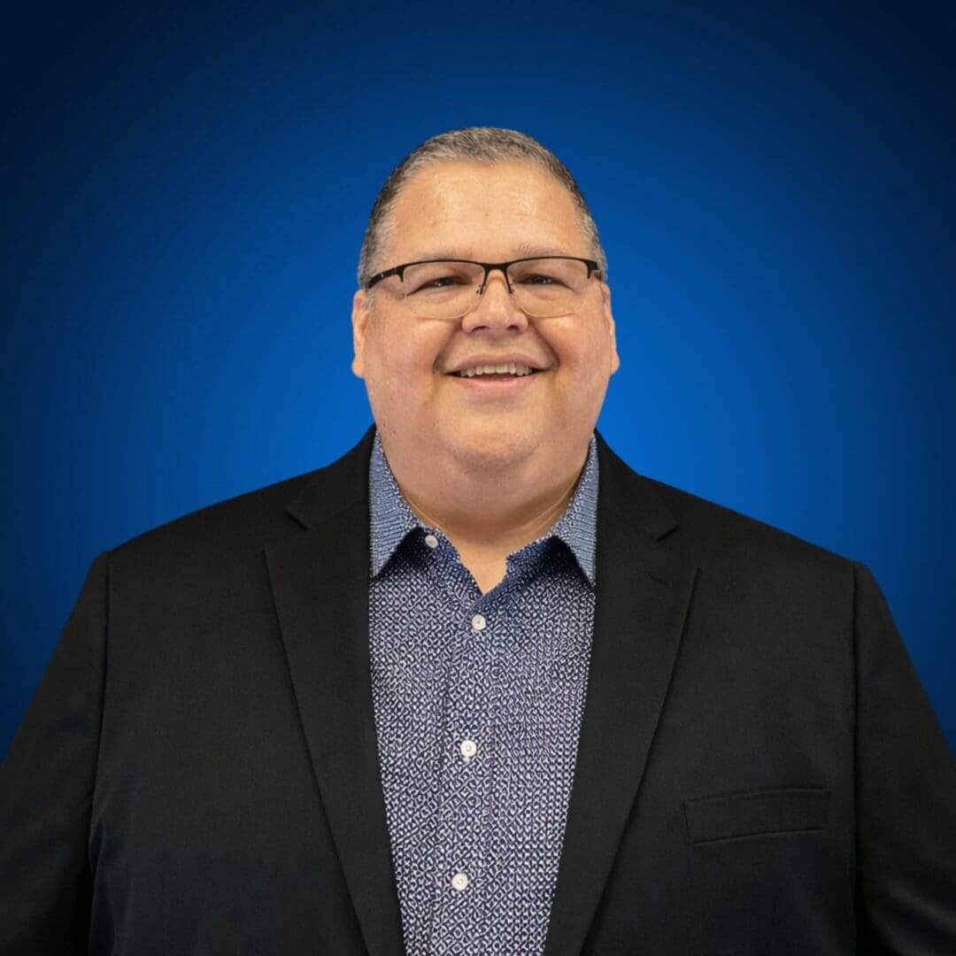 Man in suit smiling against blue background.