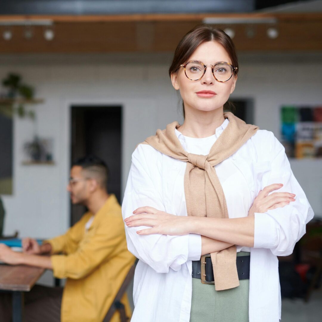 A woman wearing glasses stands confidently in front of a group of people, engaging them with her presence