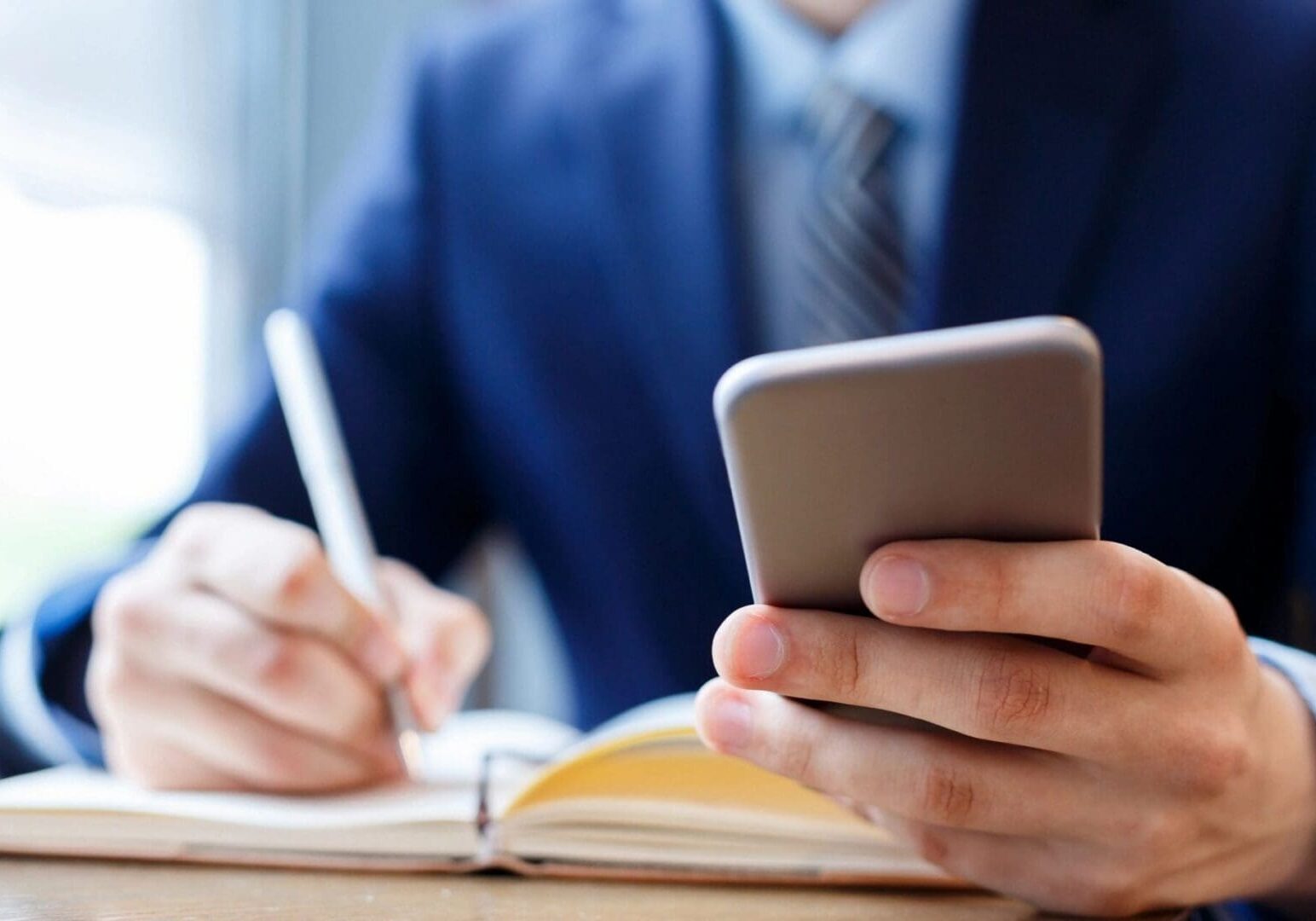 Person in suit using smartphone and notebook